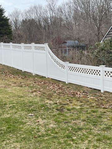 White vinyl fence with a curved dip in a grassy yard, with bare trees in the background