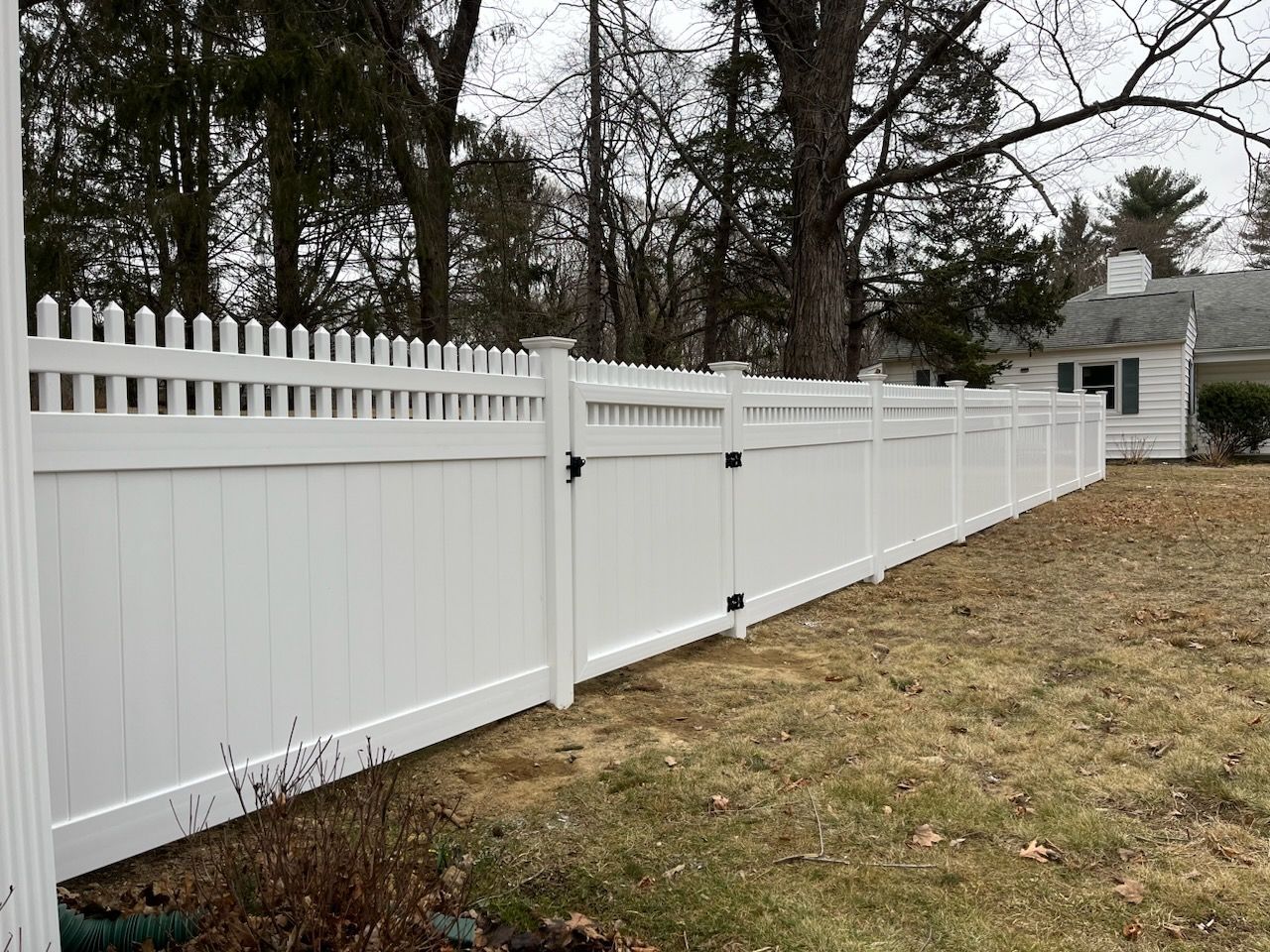 White vinyl picket fence along a grassy yard with trees in the background