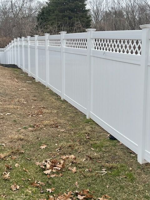Long white vinyl fence along a grassy yard with a lattice top, receding into the distance