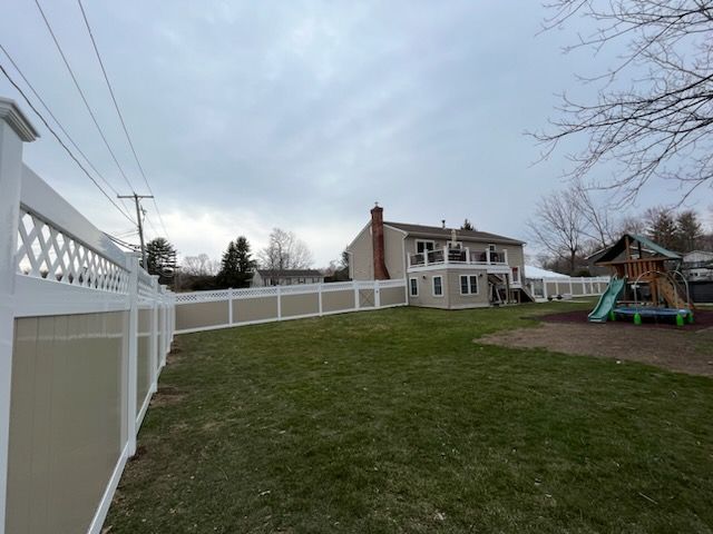Backyard with white fence, green lawn, two-story house, and a children’s playset under a cloudy sky