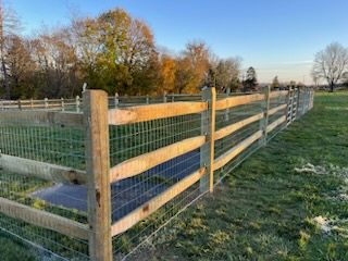 Wooden post-and-rail fence with wire mesh along a grassy path at sunset