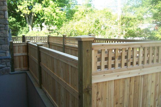Wooden privacy fence along a narrow outdoor walkway beside a stone wall and trees
