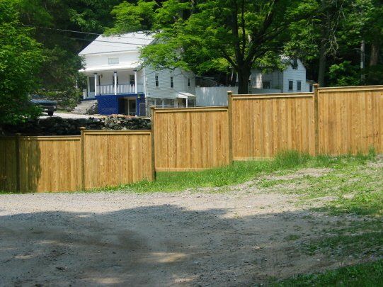Wooden fence along a dirt road with a white house and trees in the background