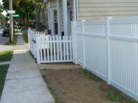White vinyl fence along a sidewalk beside a house with a small white picket gate.