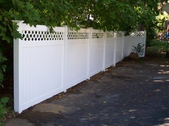 White vinyl fence along a tree-shaded driveway or walkway in a residential yard.