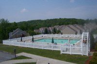 Outdoor swimming pool with white fence and lounge chairs beside a grassy hillside