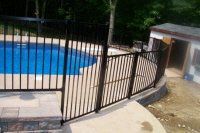 Black metal fence beside a blue pool, with a small shed and concrete patio in the background