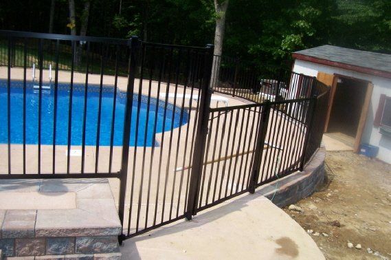 Curved black fence beside a blue swimming pool and paved patio area