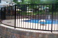 Black metal fence around a blue swimming pool in a brick courtyard with trees beyond.