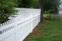 White wooden fence along a grassy yard beside trees and a driveway