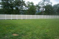 Grassy backyard with a white fence and trees in the background