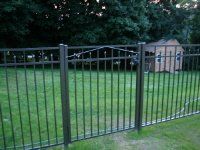 Black metal fence in a grassy yard with a small shed in the background.