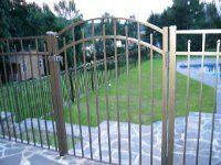 Black metal gate beside a pool and grassy yard with trees in the background
