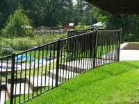 Black metal railing beside concrete steps on a grassy slope near a pool and trees