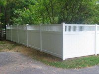 White vinyl privacy fence along a driveway beside a wooded yard.