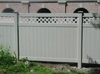 White privacy fence with lattice top in front of a brick building and greenery