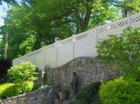 White fence atop a stone retaining wall in a leafy green park on a sunny day