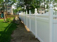 White picket fence along a dirt path beside a green lawn and trees in a residential area