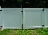 Light gray vinyl fence panels with black hinges in a grassy yard.