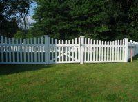 White wooden fence with an open gate in a grassy yard, backed by trees and greenery