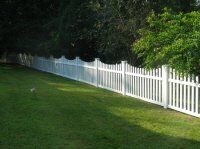 White picket fence along a green lawn beside trees in a sunny yard