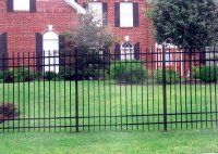 Black metal fence in front of a red brick house with a green lawn and shrubs