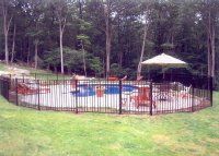 Backyard fenced-in swimming pool with red chairs and a white patio umbrella surrounded by trees