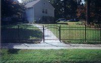 Front yard with black metal fence and open gate leading to a walkway and house beyond.