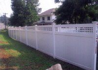 White vinyl privacy fence lining a grassy yard in front of a house with trees