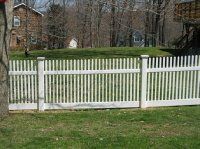 White wooden fence along a grassy park edge with trees and brick buildings in the background