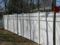 White vinyl privacy fence along a yard with tree shadows in daylight
