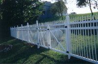 White picket fence along a grassy hillside with trees in the background