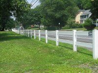 White fence along a grassy roadside in a suburban neighborhood on a sunny day