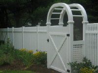 White garden arbor gate in front of a white picket fence and greenery