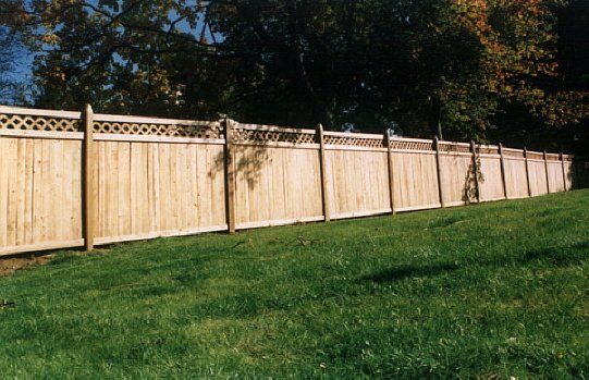 Long wooden privacy fence along a green grassy yard with trees behind it.