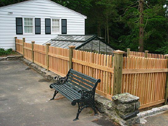 Bench beside wooden fence and white house with black shutters on a roadside corner