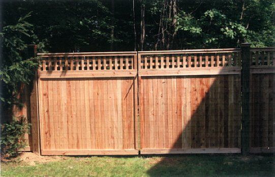 Wooden privacy fence gate with lattice top in a shaded backyard.