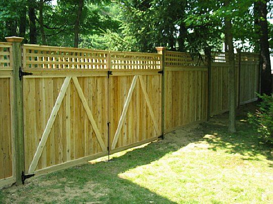 Wooden backyard fence with a double gate and lattice top, set beside a grassy yard and trees.