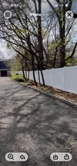 Tree-lined driveway beside a white fence leading to a house on a sunny day