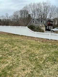 White vinyl fence curving along a grassy yard beside a gray house and parked car on an overcast day