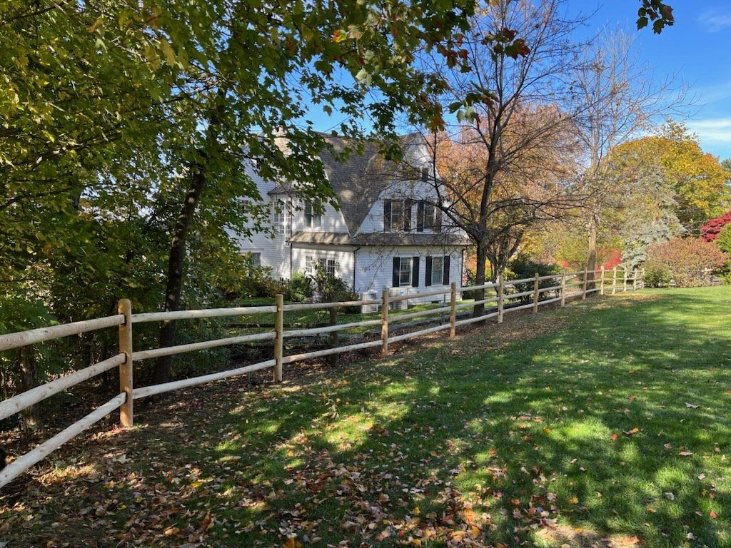 White farmhouse behind a wooden fence along a leafy path in autumn sunlight
