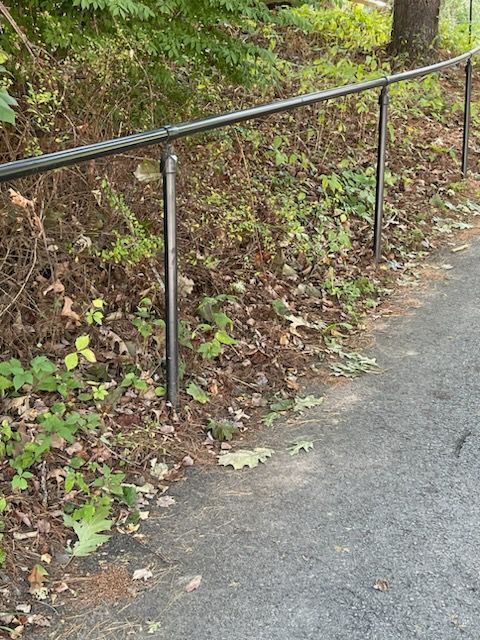 Black metal handrail along a sloped, leaf-covered hillside beside a paved path.