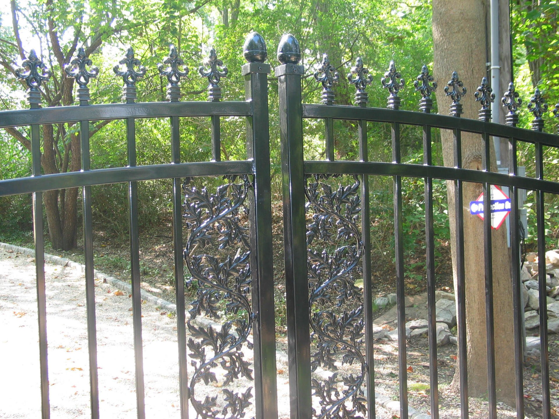 Black wrought-iron gate with arched top in front of a leafy garden path