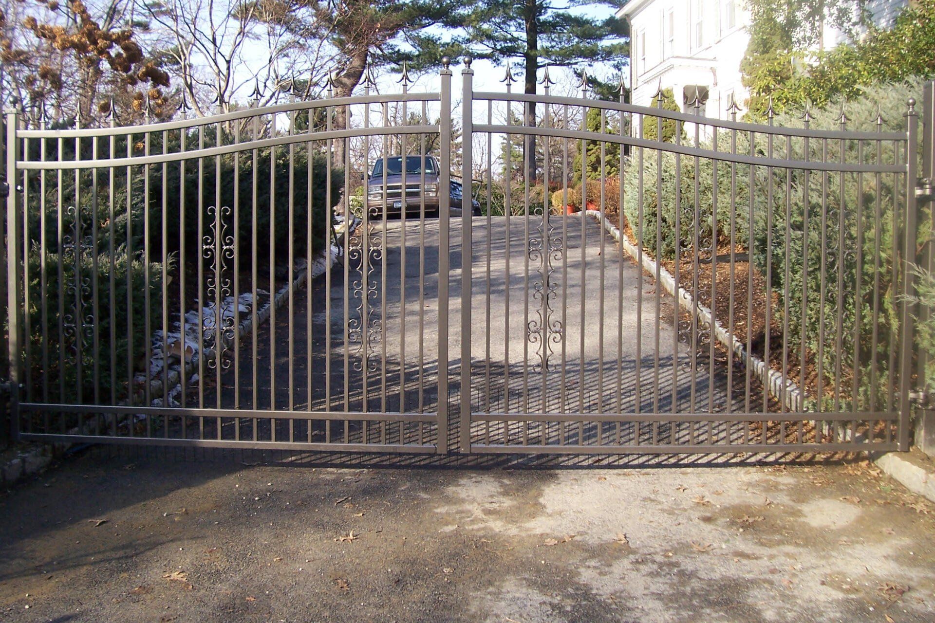 Closed metal driveway gate at the end of a tree-lined driveway with a house in the background