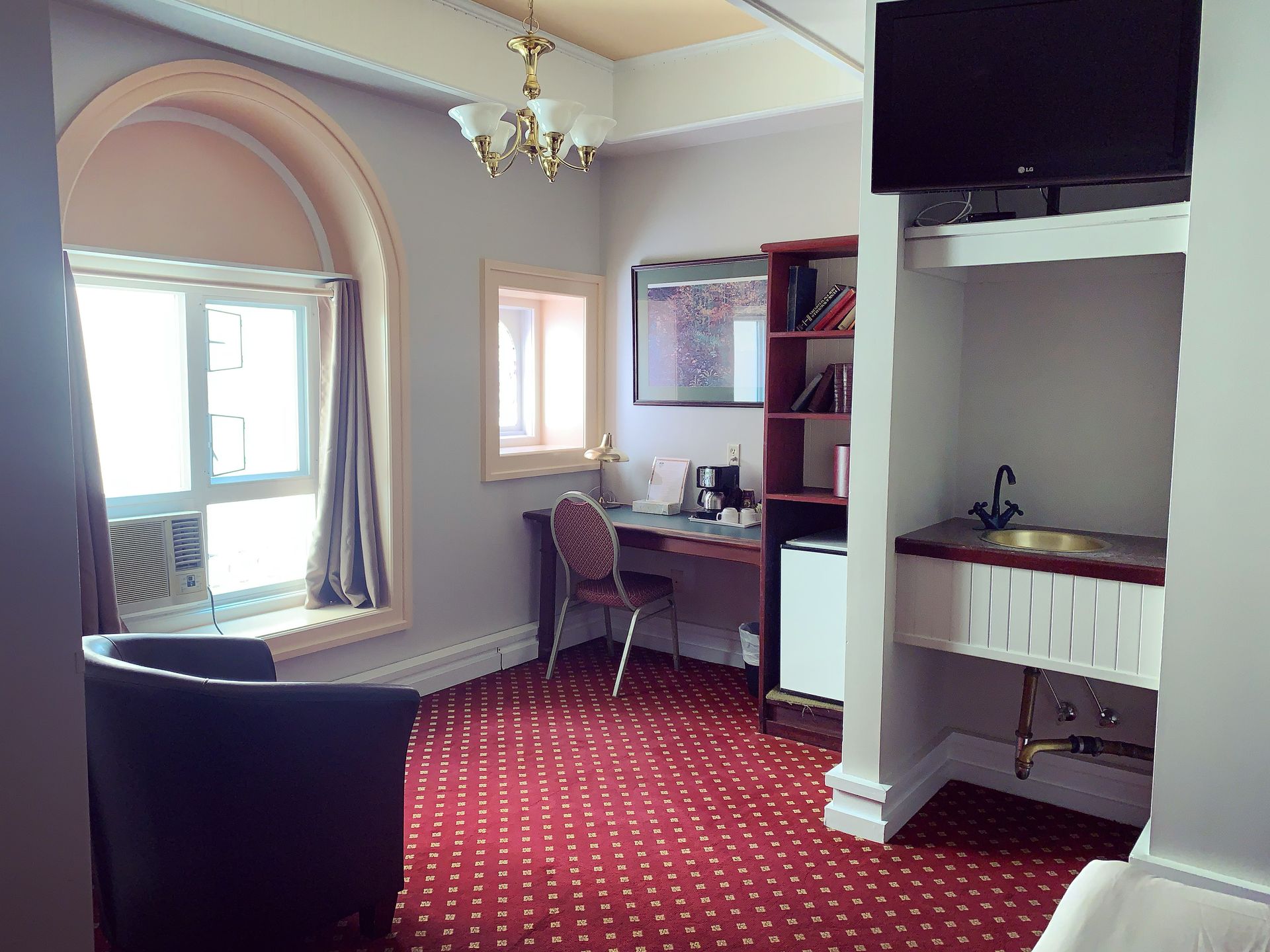 A hotel room with a chair a desk and a television