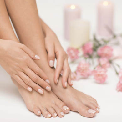Mani con unghie rosa pallido appoggiate su piedi nudi accanto a candele e fiori