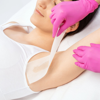 Durante un trattamento di epilazione, delle mani guantate applicano una striscia di cera bianca sotto l'ascella di una donna.