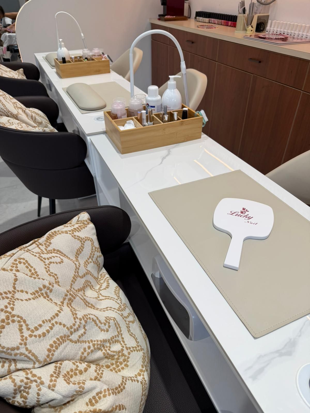 Postazione per manicure in salone con tavolini bianchi, strumenti per unghie e una sedia nera accanto a una seduta imbottita.