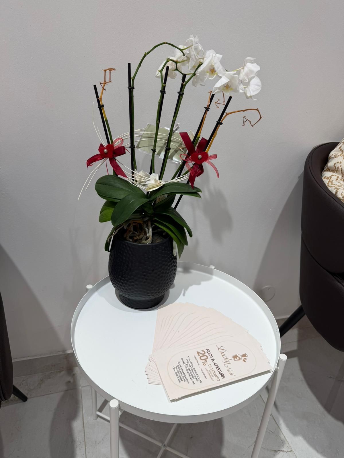Orchidea bianca in vaso nero su un tavolino rotondo, con un menù accanto.