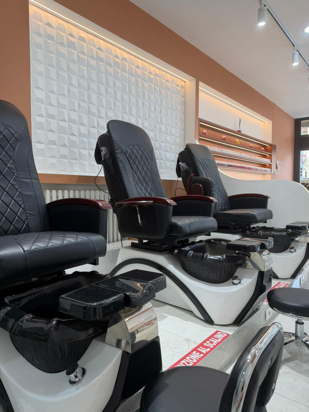 Una fila di poltrone nere per pedicure e bacinelle per i piedi in un luminoso interno di un salone.
